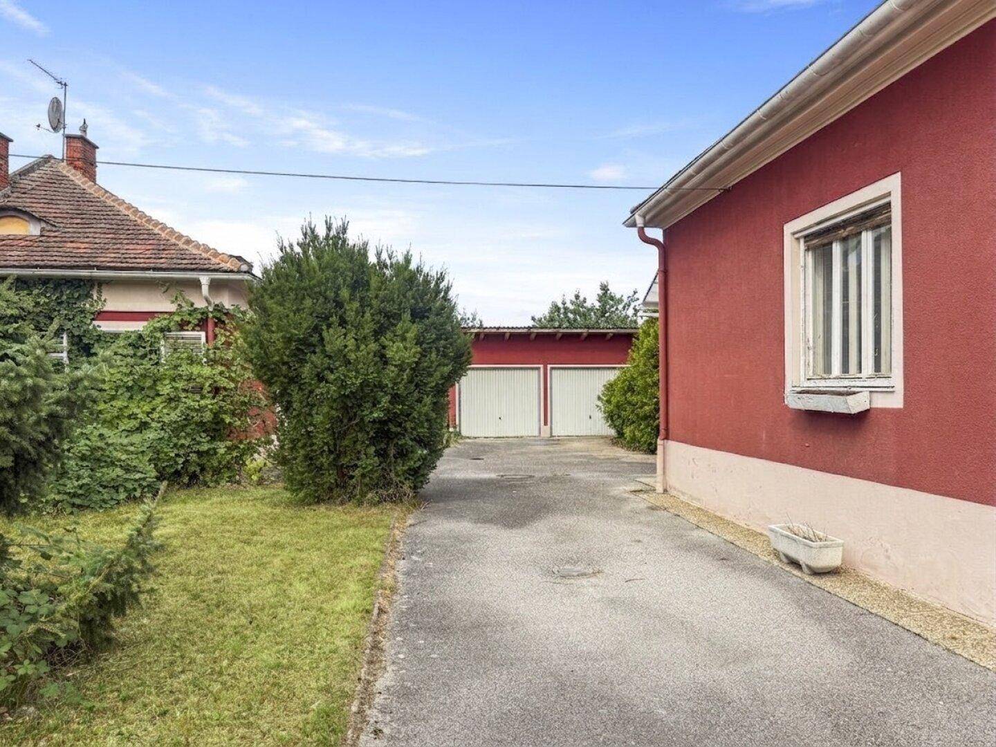 Zufahrt zum Haus mit Garagen im Hintergrund und gepflegter Grünfläche.