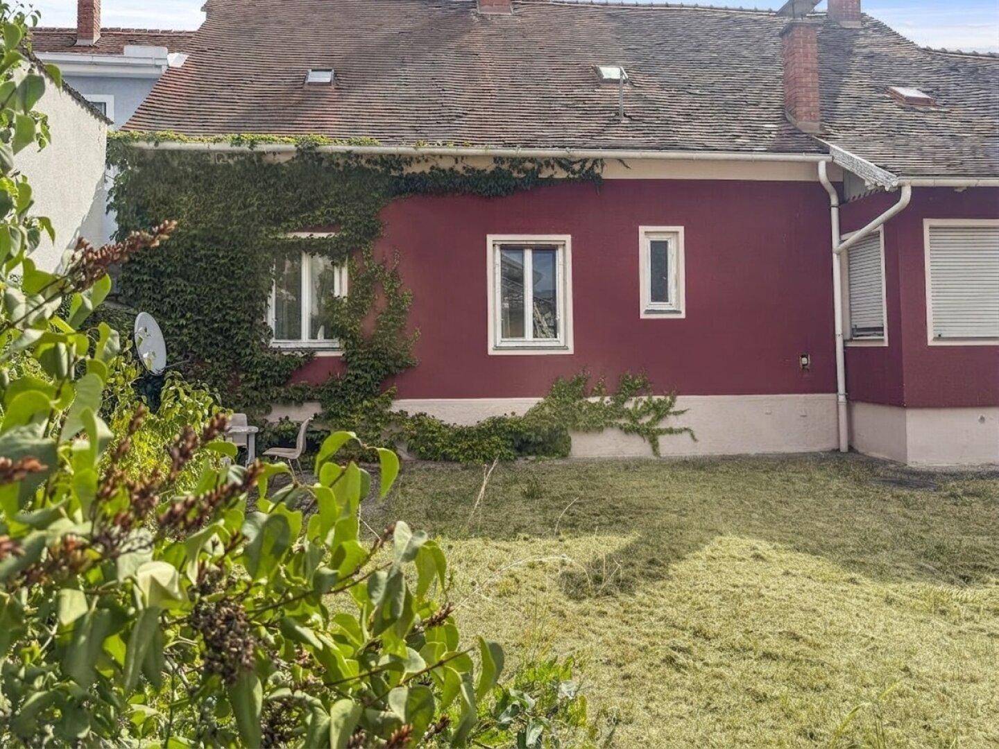Gartenbereich mit frisch gemähtem Rasen, grünen Büschen und der roten Hausfassade.