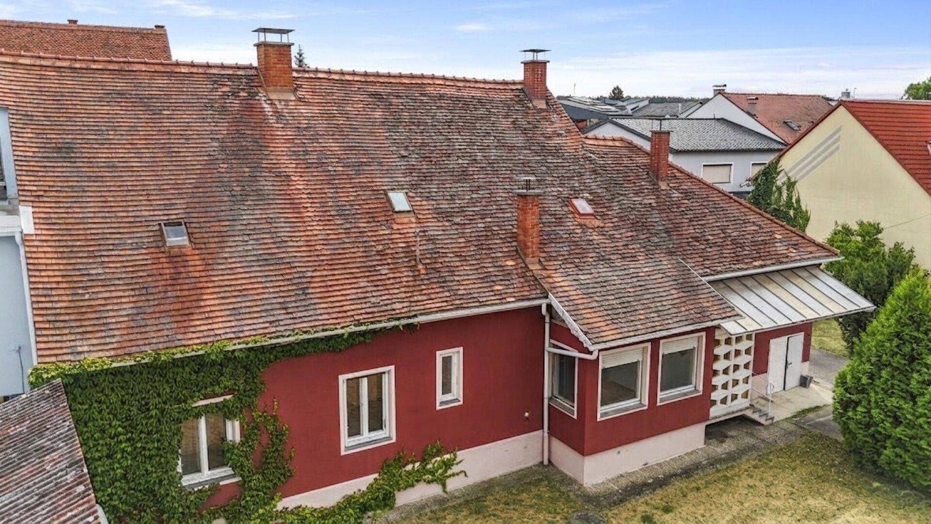 Rückansicht des roten Hauses mit Fenstern, Efeubewuchs und dem Ziegeldach unter blauem Himmel.