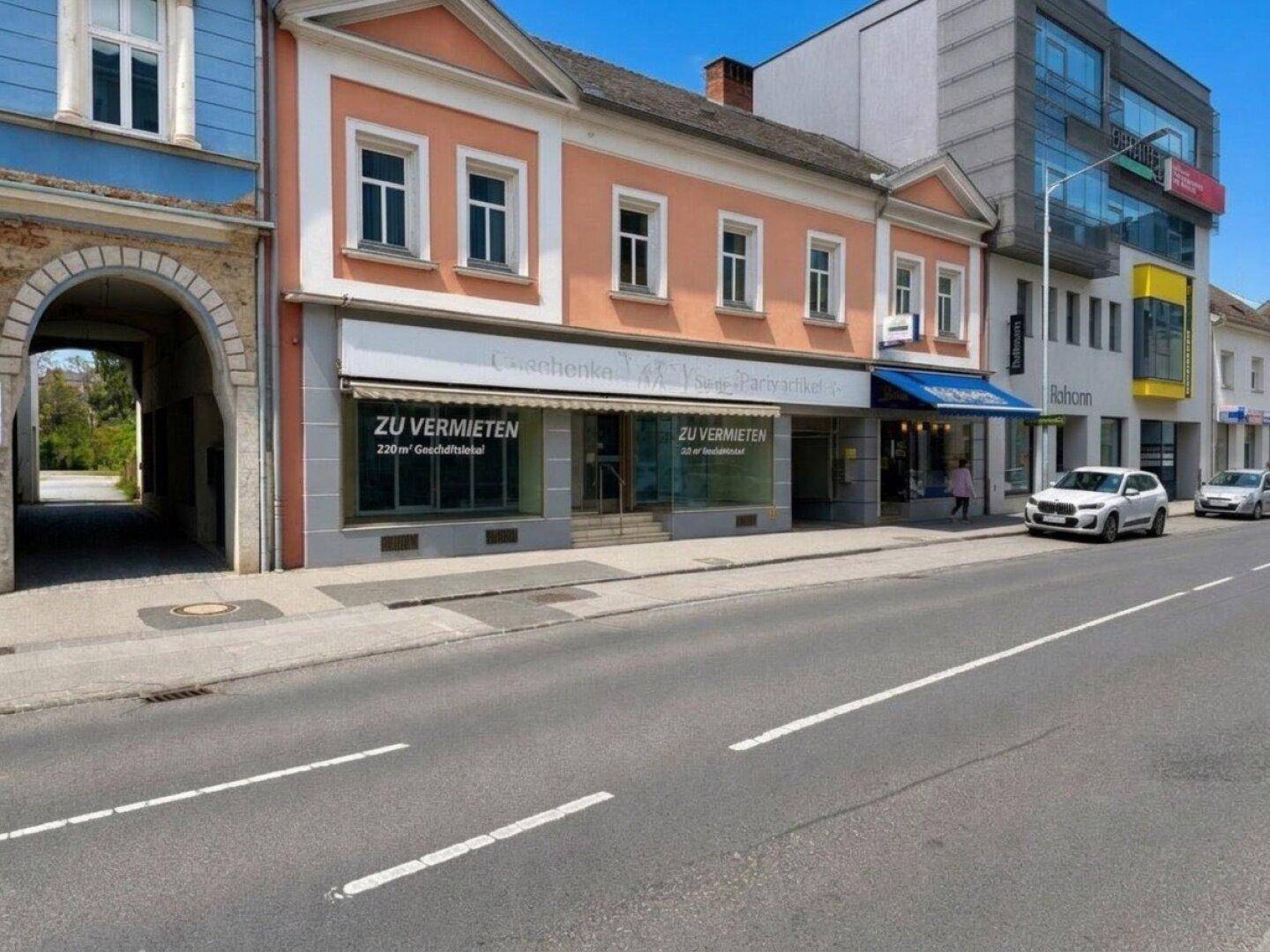 Blick auf die Straßenseite des Gebäudes mit angrenzenden Häusern und parkenden Autos, unter blauem Himmel.