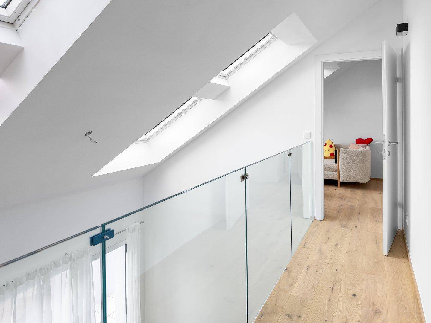 Offene Galerie mit Glasgeländer, Holzfußboden und Dachfenstern im Dachschrägenbereich.