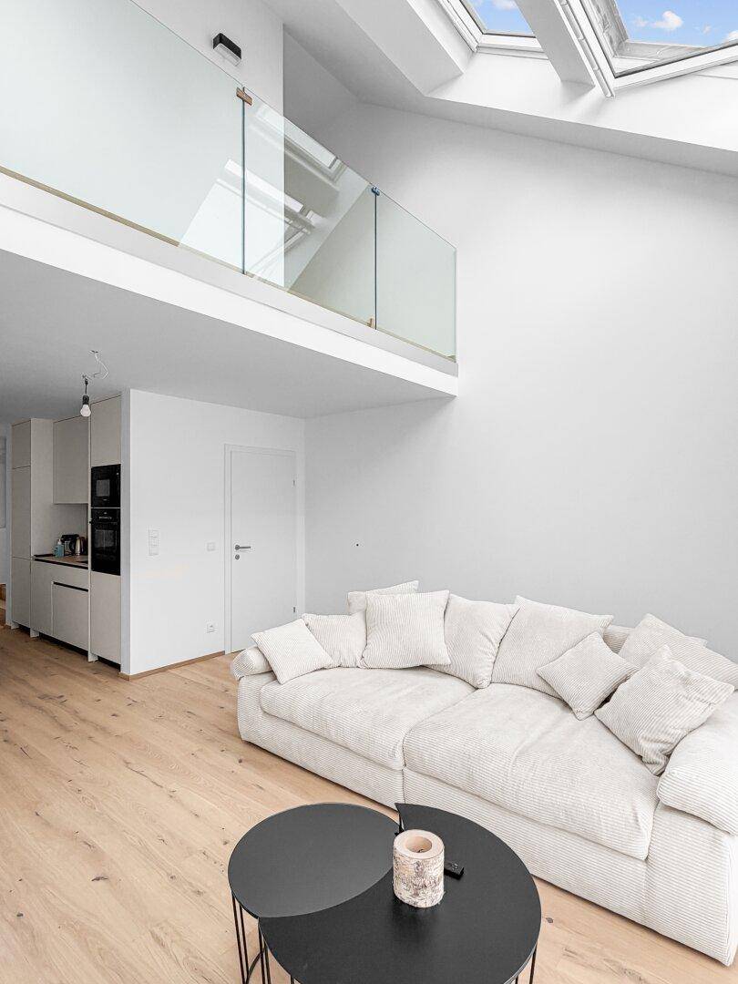 Offener Wohnbereich mit hohen Decken, Dachfenstern und einer modernen Galerie mit Glasbrüstung.