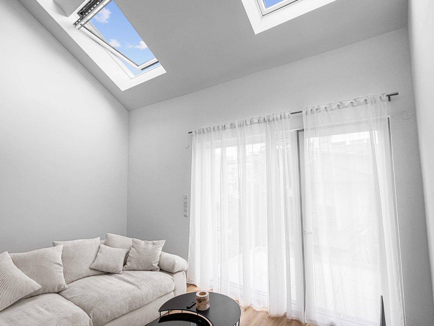 Heller Wohnraum mit gemütlichem Sofa, Holzfußboden und mehreren Dachfenstern für viel Tageslicht.