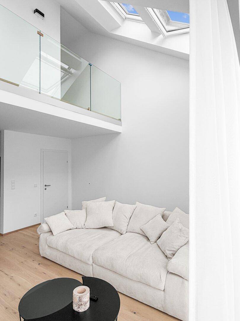 Lichtdurchfluteter Wohnbereich mit hohen Decken, Dachfenstern und einer modernen Galerie mit Glasgeländer.
