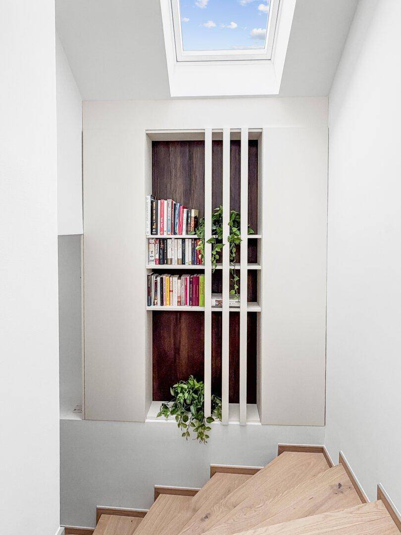 Holztreppe mit integriertem Bücherregal, Pflanzen und einem Dachfenster für natürliches Licht.