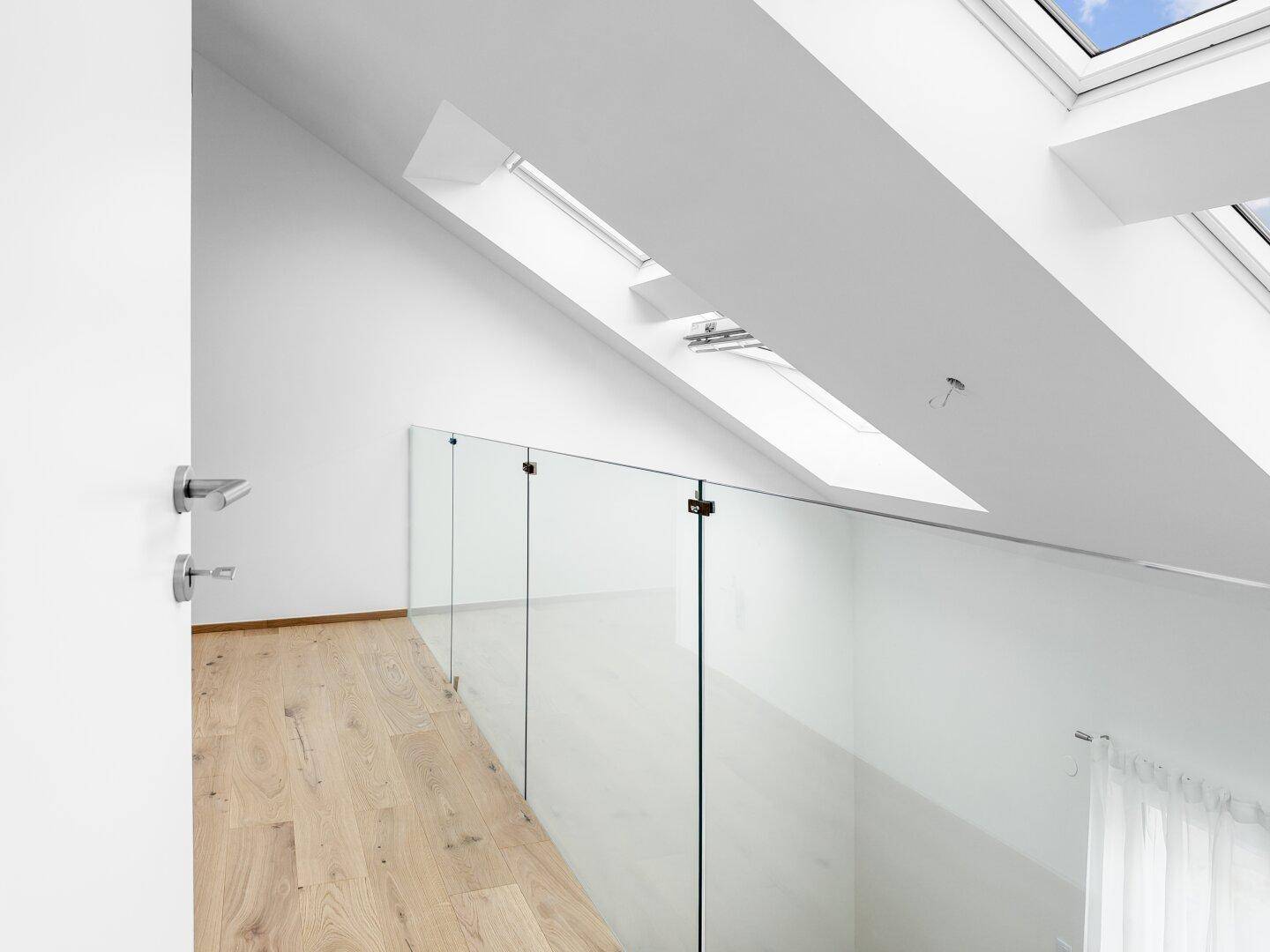 Helle Galerie mit Glasgeländer, Holzfußboden und mehreren Dachfenstern in der Dachschräge.