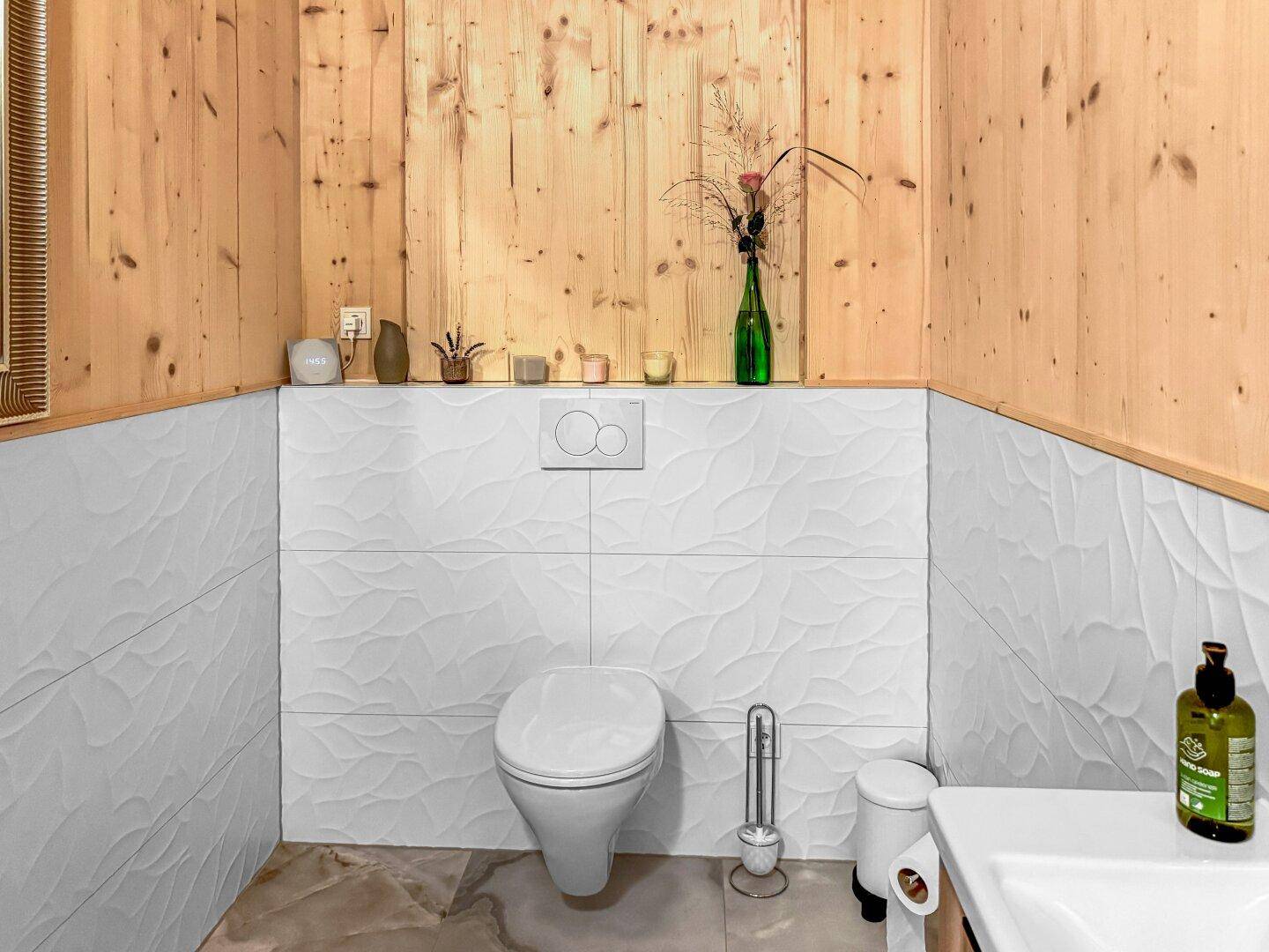 Modernes Gäste-WC mit wandhängender Toilette, Waschbecken und strukturierten Fliesen.