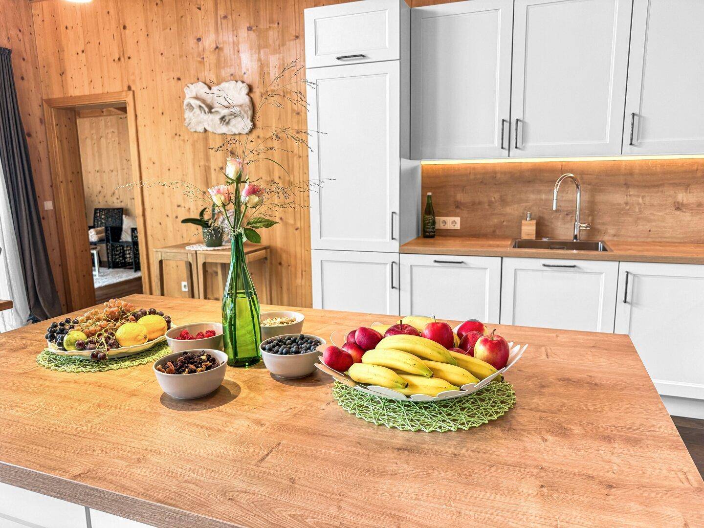 Kücheninsel mit Holzplatte und frischen Früchten, umgeben von weißen Küchenschränken und Holzwänden.