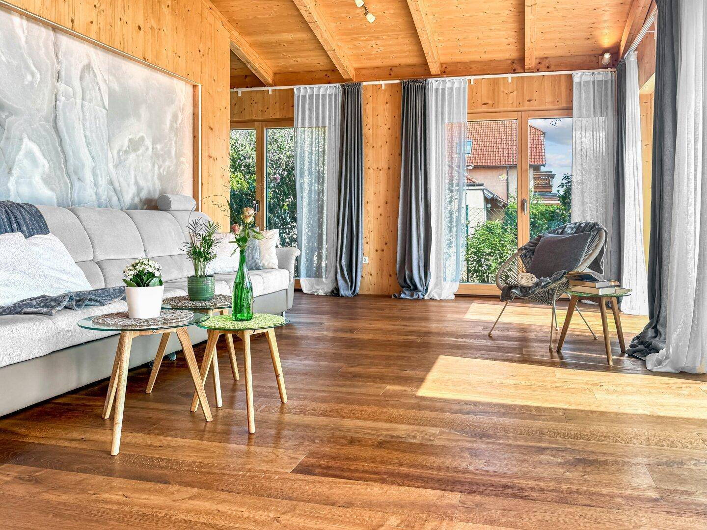 Helles Wohnzimmer mit Holzwänden, Holzboden und großen Fenstern, die viel Tageslicht hereinlassen.