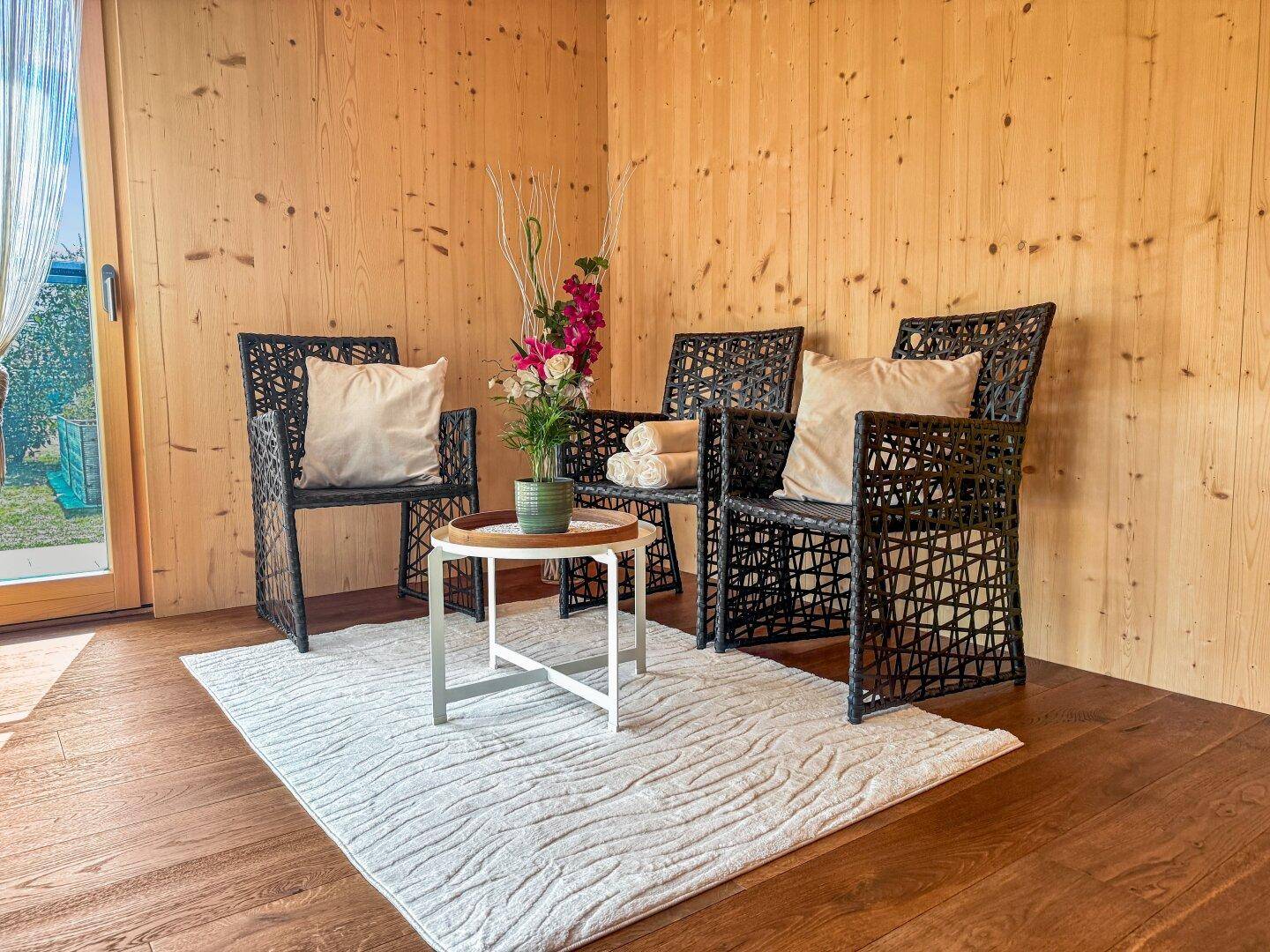 Kleine Sitzecke mit Korbstühlen und Teppich, umgeben von Holzwänden.