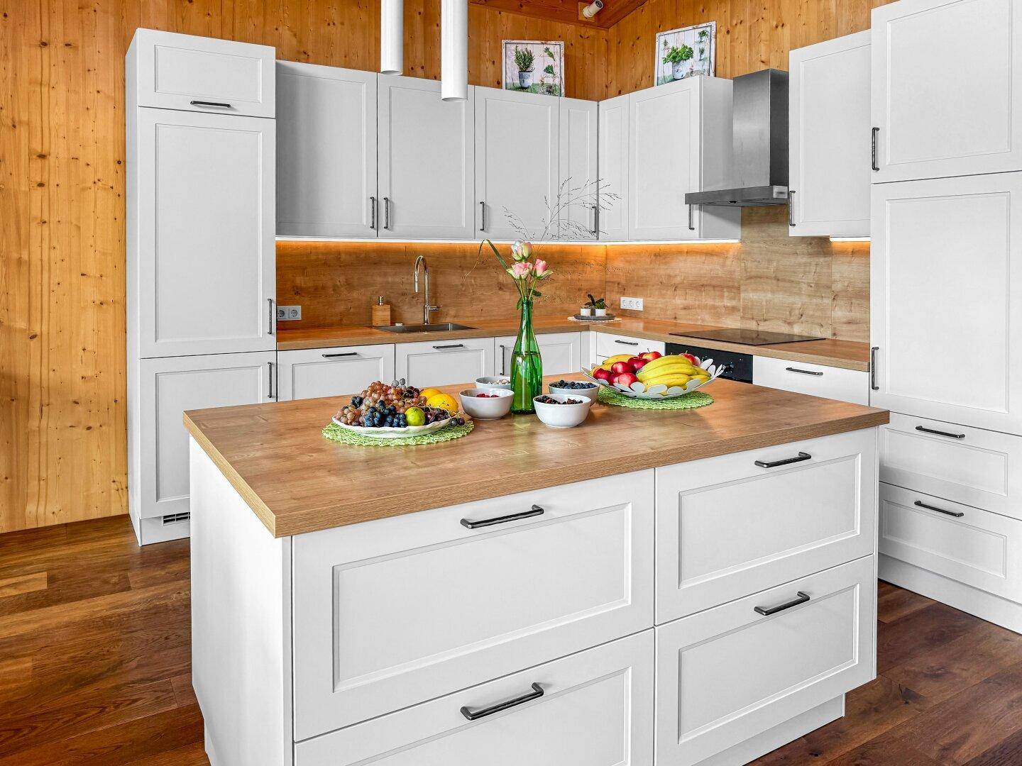 Moderne Küche mit weißen Schränken, Holztheke und Kücheninsel, umgeben von Holzwänden.