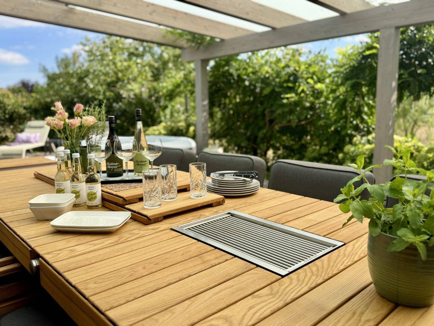 Gedeckter Esstisch auf der Terrasse mit Geschirr und Getränken, bereit für eine Mahlzeit im Freien.