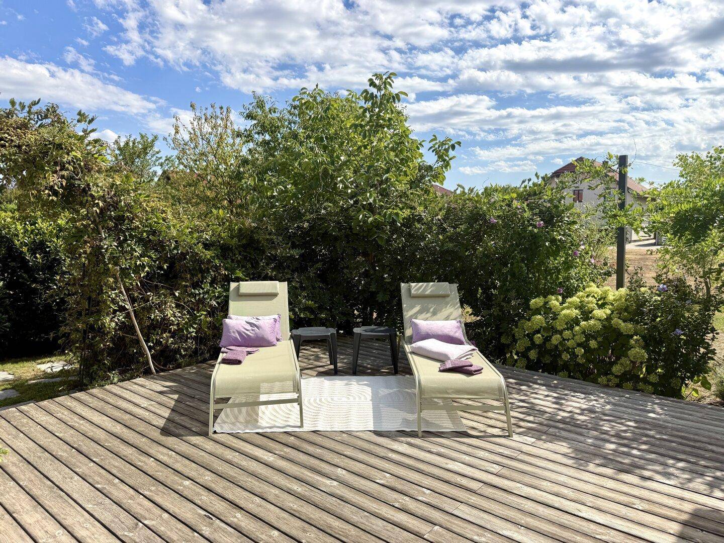 Entspannungsbereich auf der Holzterrasse mit zwei Liegestühlen und Kissen unter blauem Himmel.
