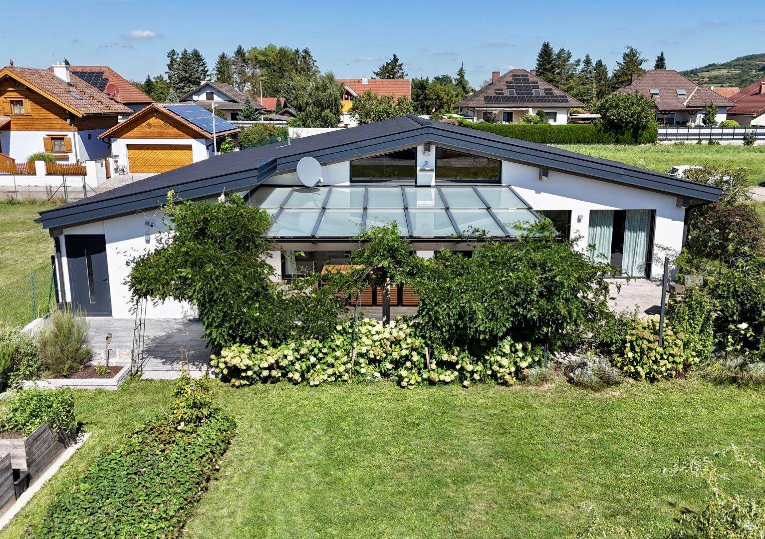 Modernes Einfamilienhaus mit großem Garten, Glasdach und umliegender Natur in ländlicher Umgebung.