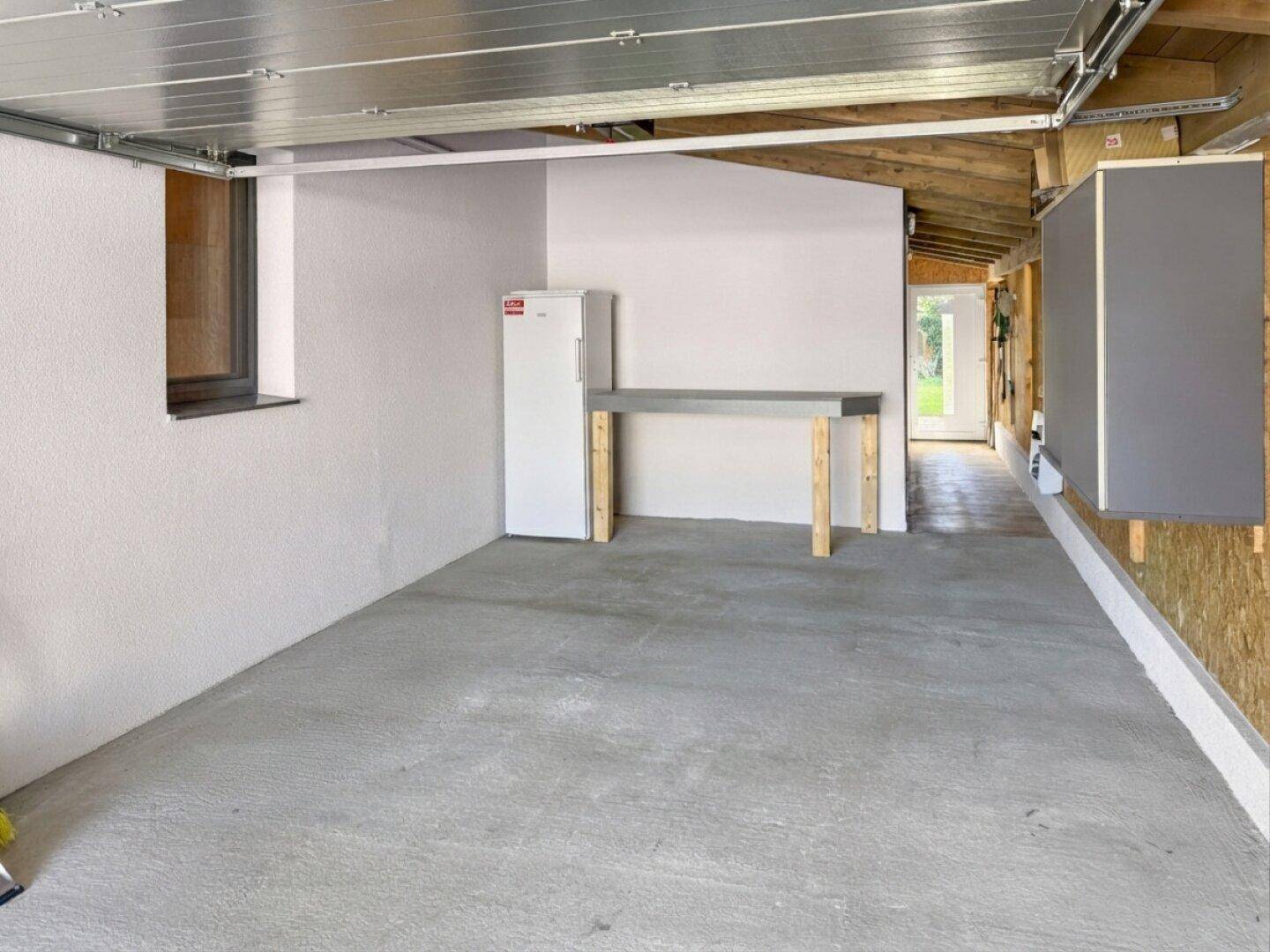 Geräumige Garage mit Betonboden, weiß gestrichenen Wänden und einem Kühlschrank.