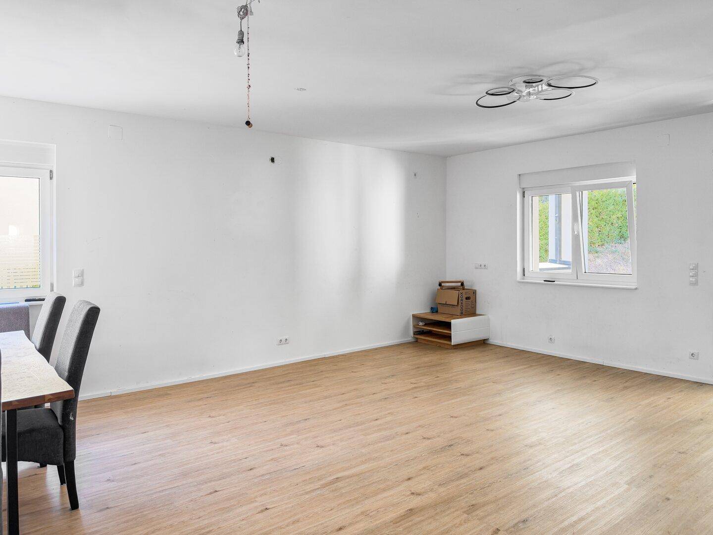 Heller Wohnbereich mit Laminatboden und großen Fenstern, bietet viel Platz für individuelle Einrichtung.