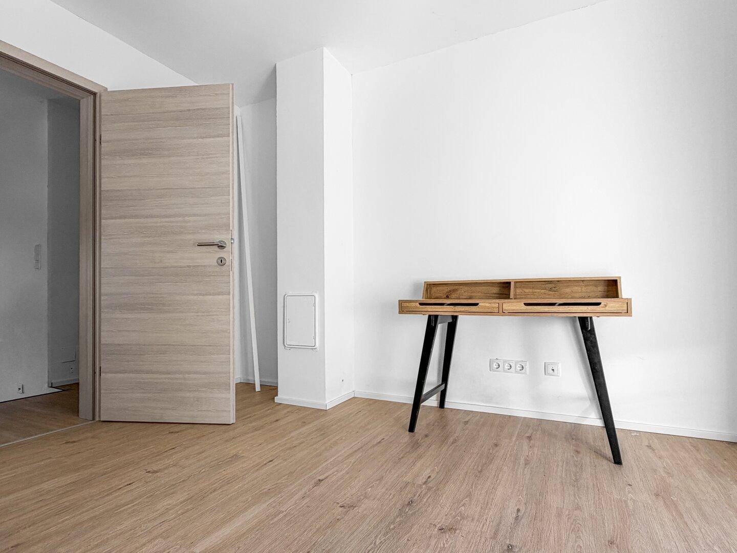Helles Zimmer mit Holzboden und einem modernen Holzschreibtisch, ideal als Arbeitszimmer.