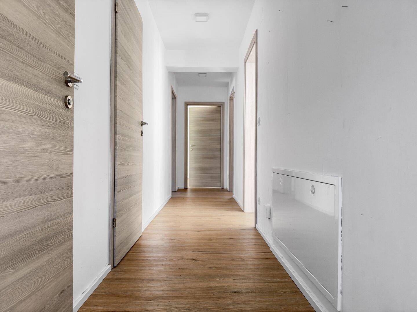 Langer, heller Flur mit Holzböden und modernen Holztüren, der zu verschiedenen Räumen führt.