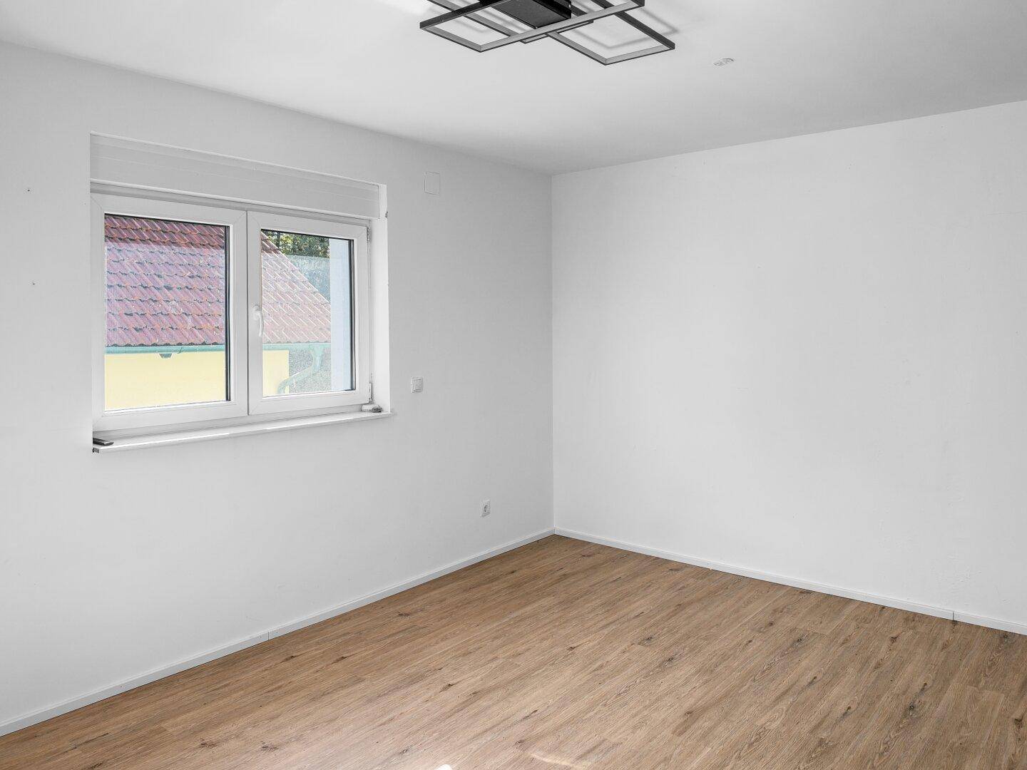 Helles Zimmer mit Holzboden und einem Fenster, das viel Tageslicht hereinlässt.