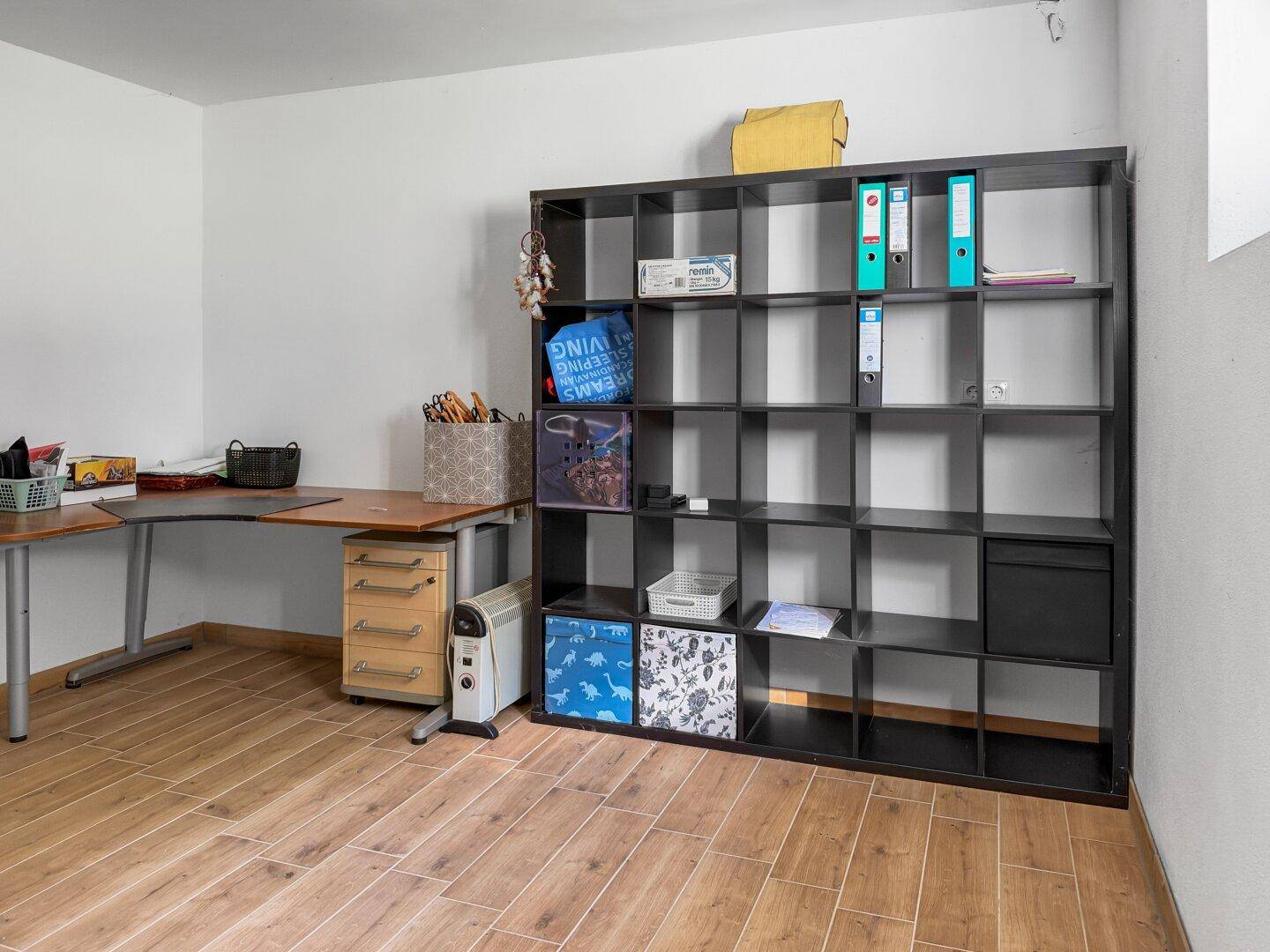 Kellerraum als Büro oder Lager genutzt, mit Schreibtisch und großem Regal, gefliest.