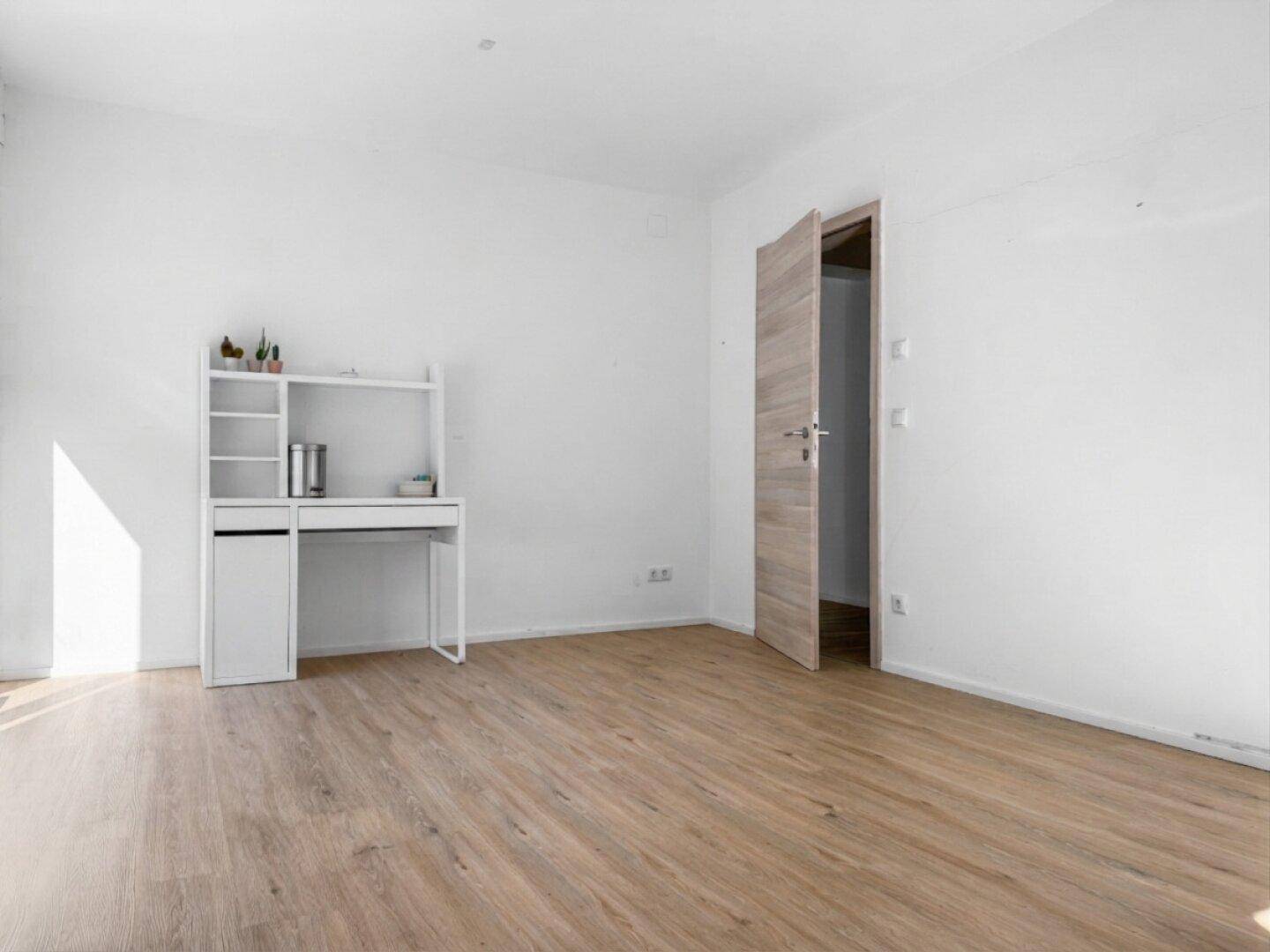 Helles Zimmer mit Holzboden und einem weißen Schreibtisch mit Regal, ideal als Arbeitsbereich.