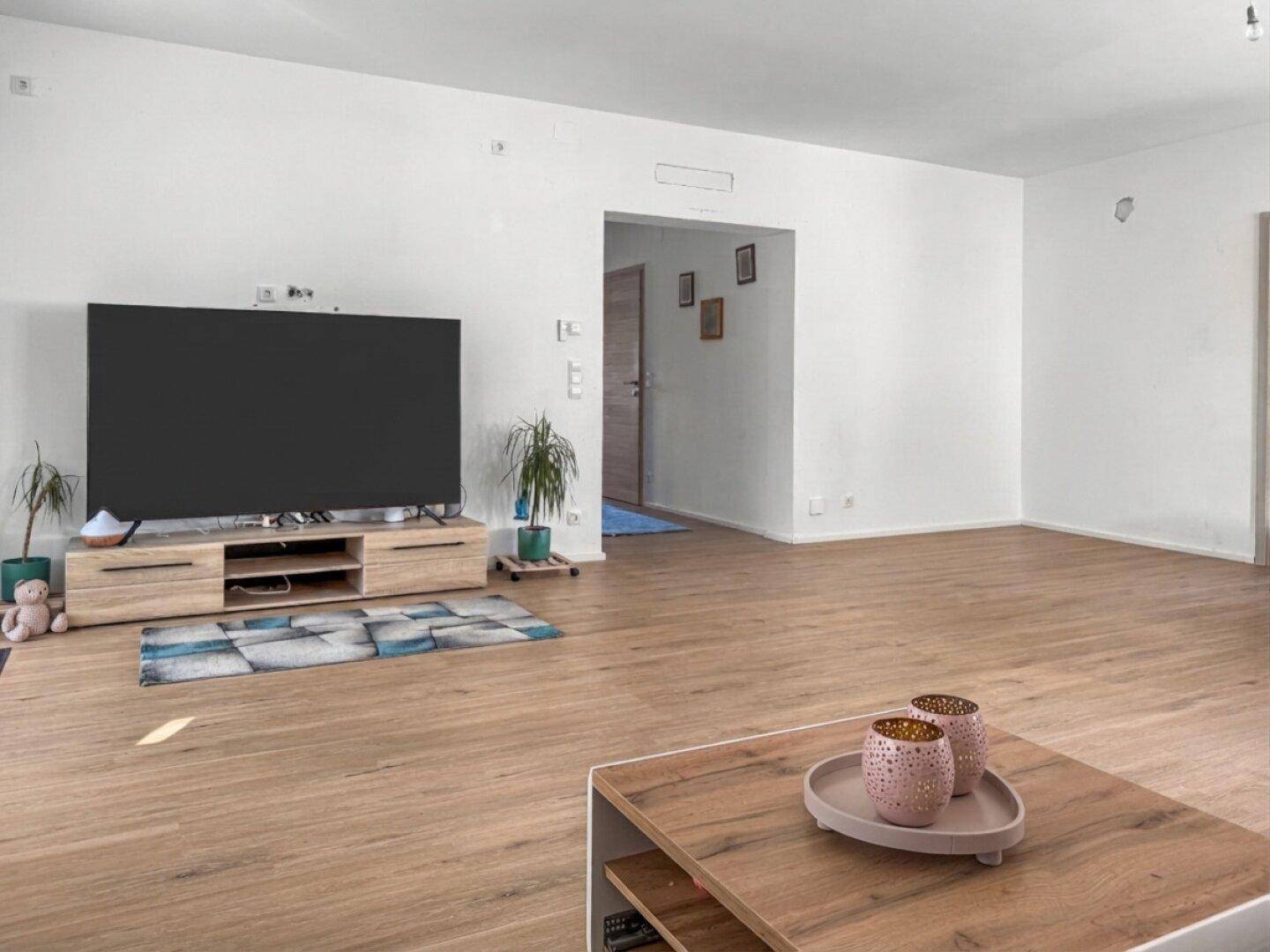 Geräumiges Wohnzimmer mit hellem Laminatboden und viel Tageslicht, ideal für Entspannung.