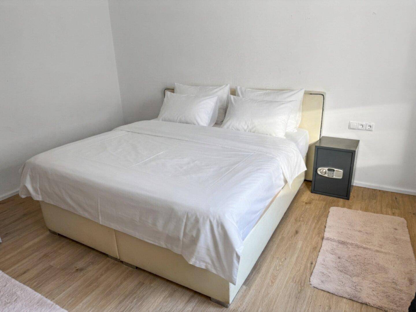 Helles Schlafzimmer mit großem Bett, weißer Bettwäsche und hellem Laminatboden.