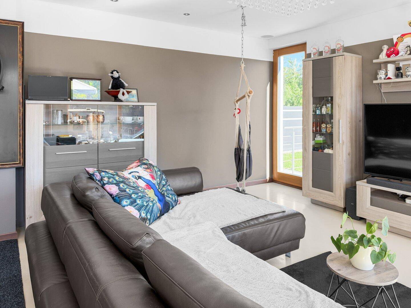 Helles Wohnzimmer mit dunklem Sofa und Hängesessel, mit Zugang zum Außenbereich.