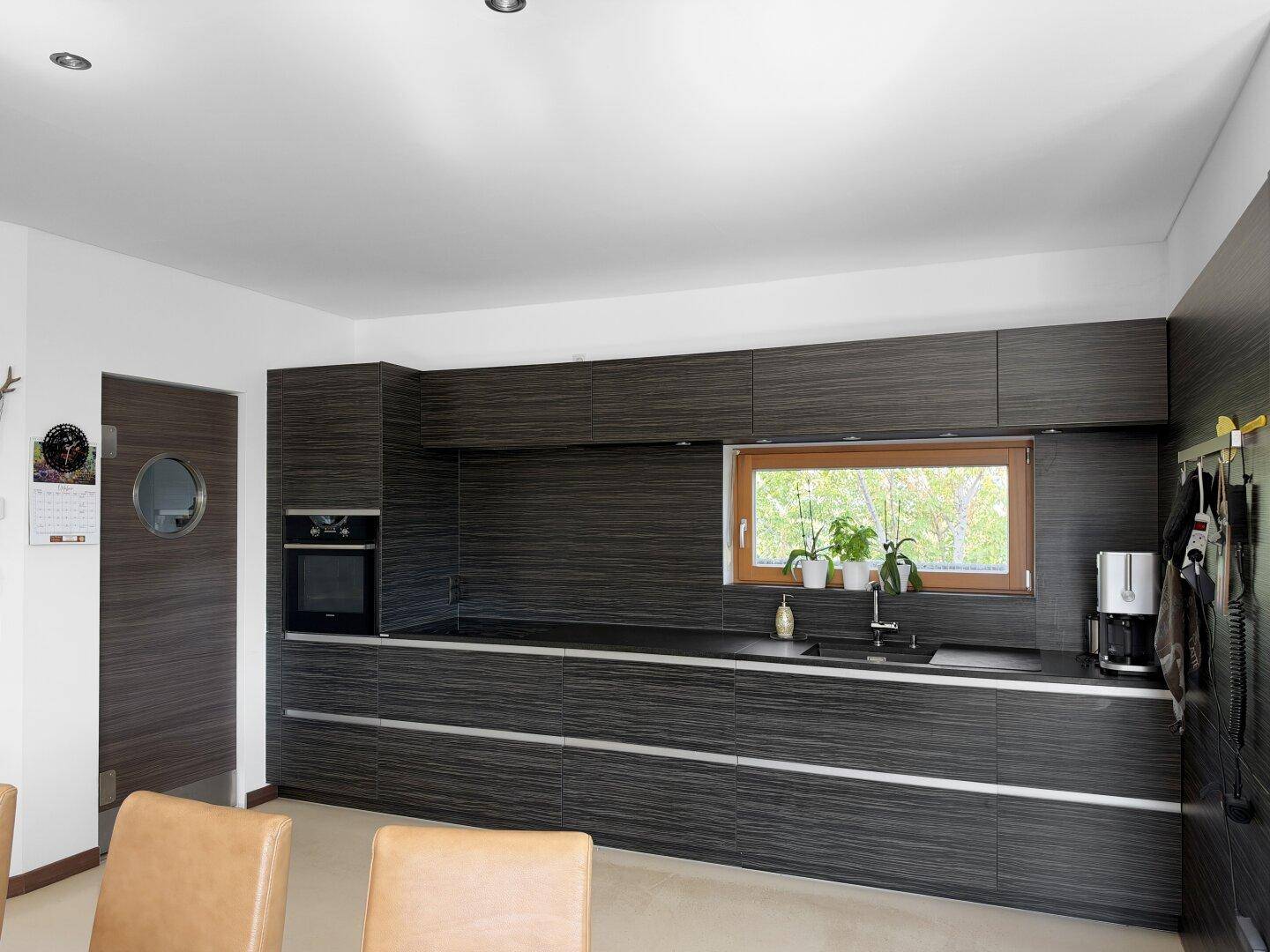 Stilvolle Küche mit dunklen Holzfronten, Backofen und einem Fenster für natürliches Licht.