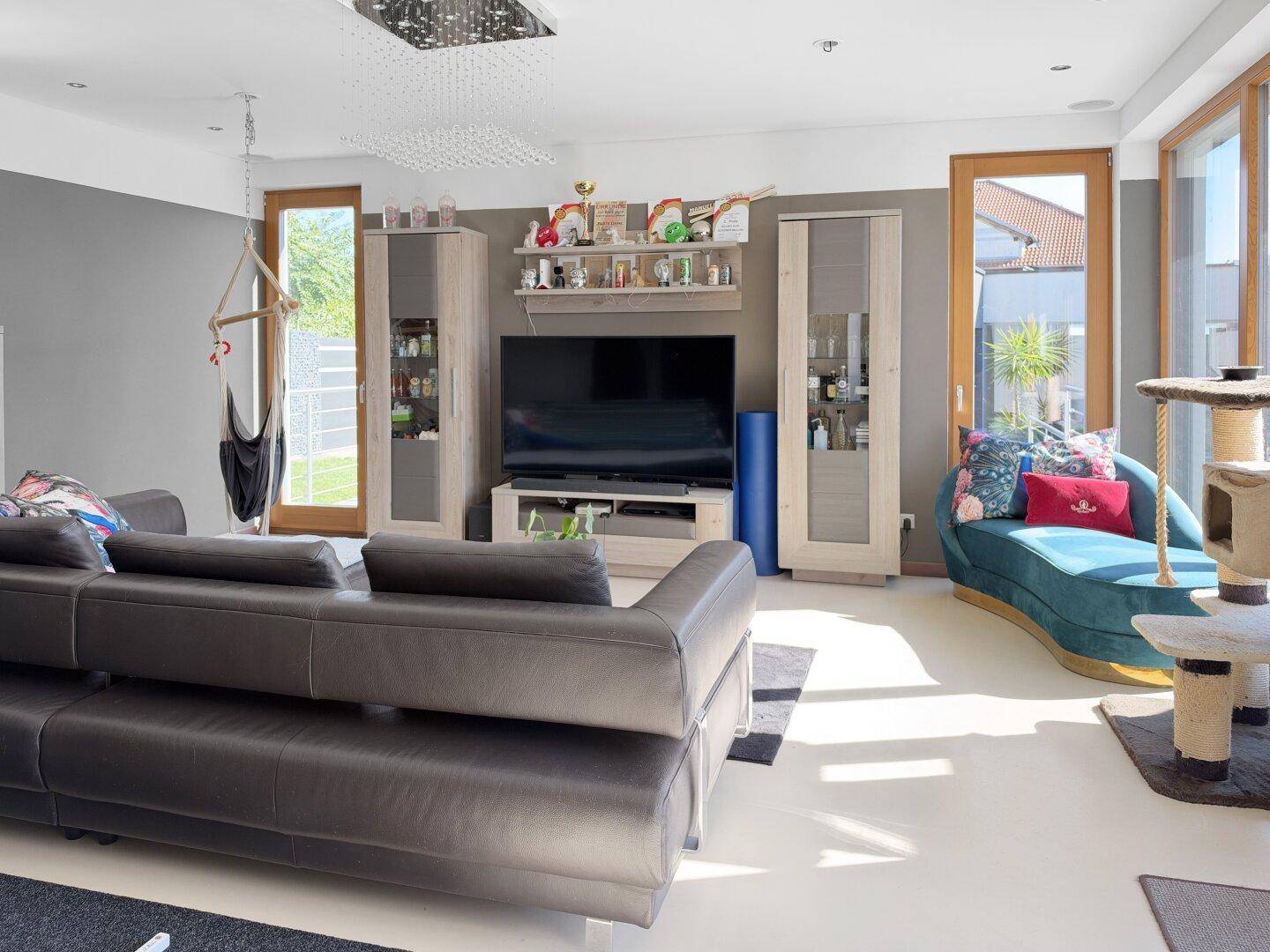 Modernes Wohnzimmer mit großem Fernseher und viel Tageslicht durch die Fensterfront.
