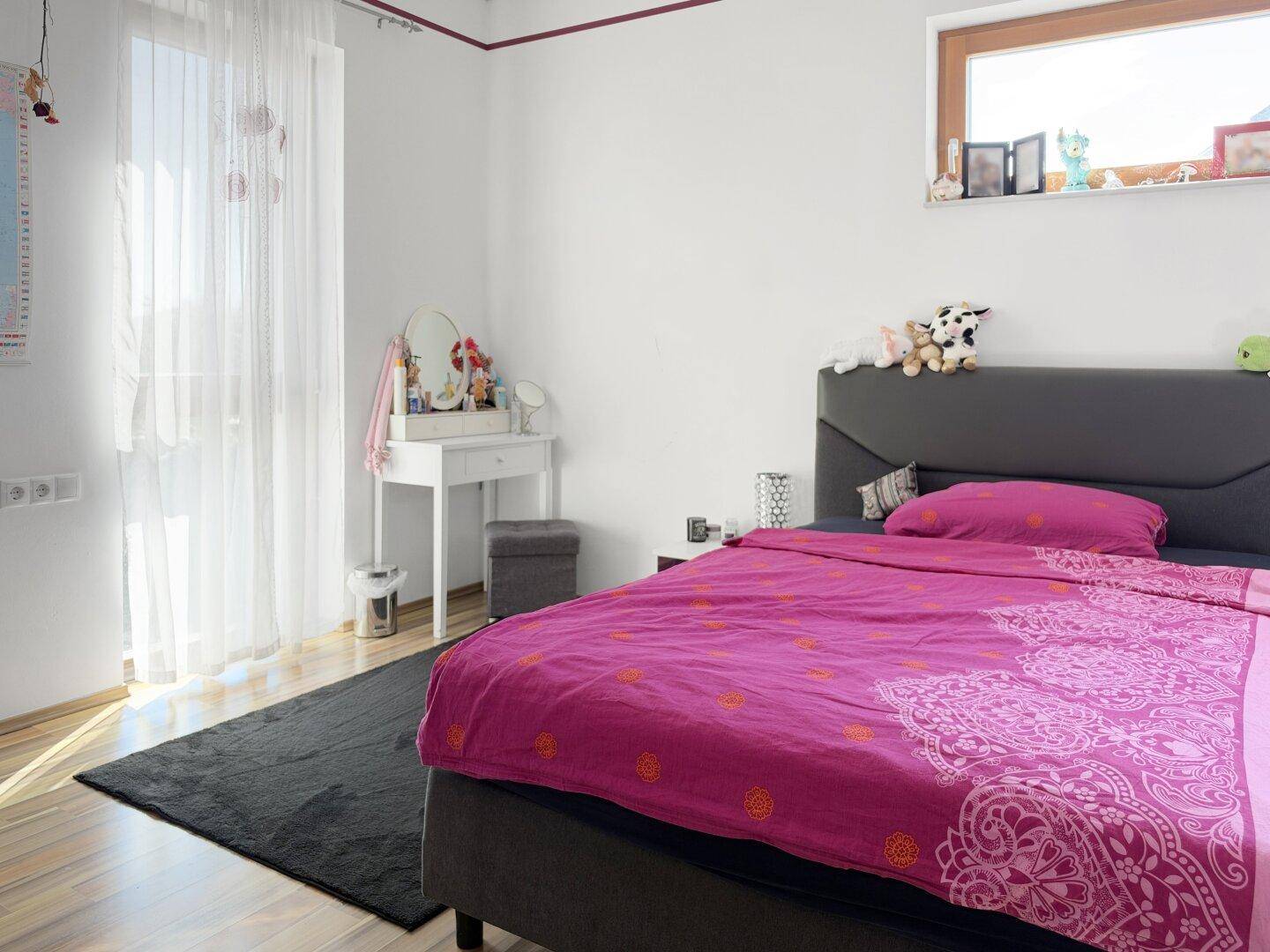 Helles Schlafzimmer mit Bett, Schminktisch und großem Fenster für viel Tageslicht.