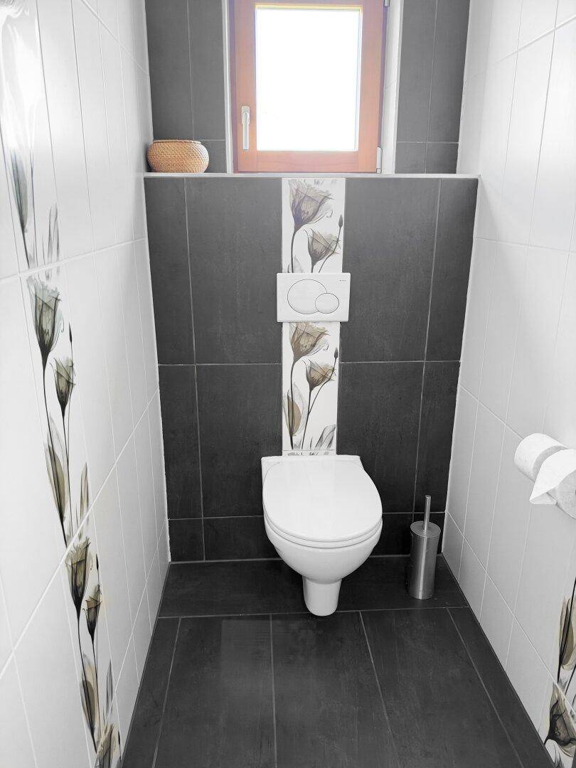 Modernes WC mit wandhängender Toilette, dunklen und hellen Fliesen und Fenster.