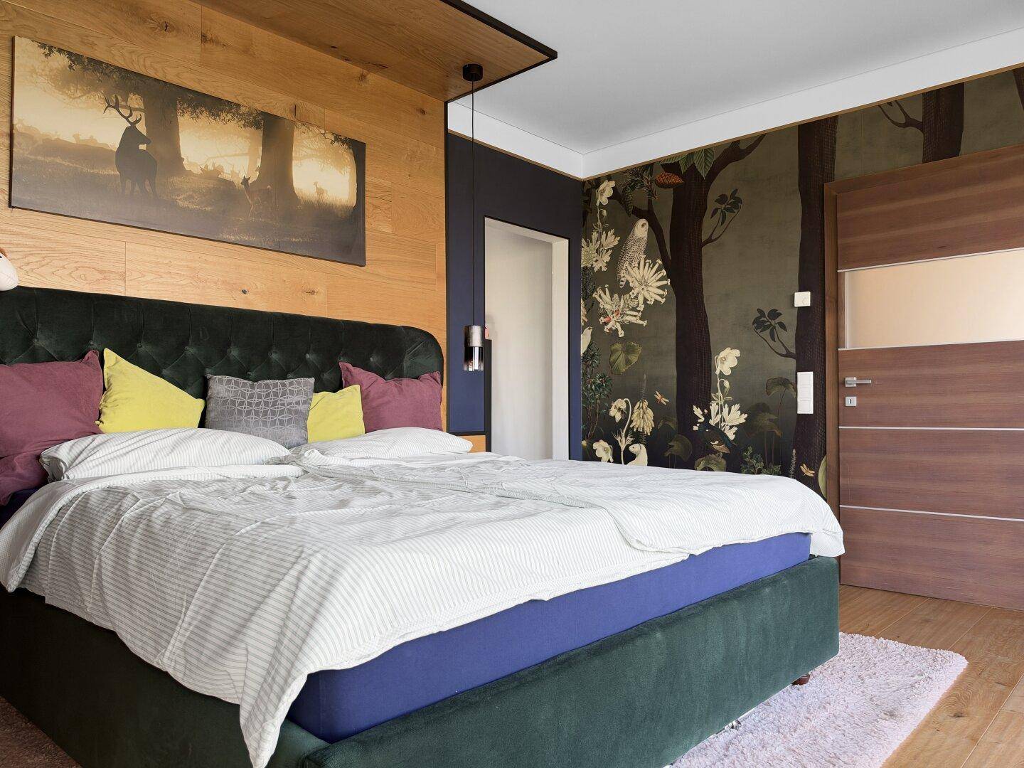 Stilvolles Schlafzimmer mit großem Bett, Holzwand und dekorativer Tapete mit Waldmotiv.