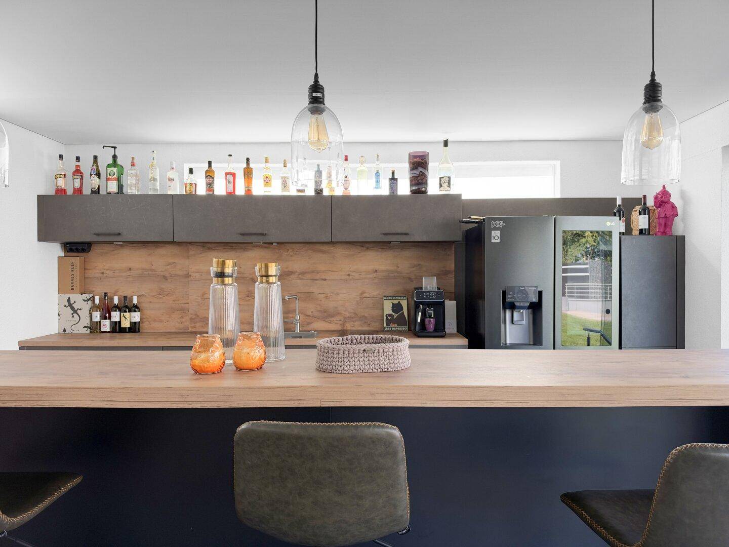 Detailansicht der modernen Küchenbar mit Holzplatte, Barhockern und dekorativen Elementen.