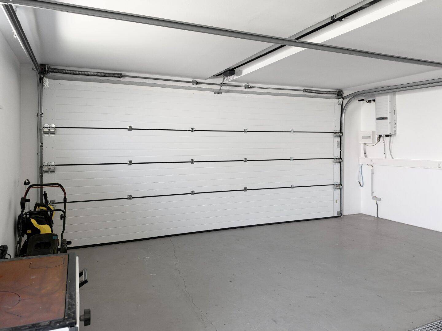 Geräumige Garage mit weißem Sektionaltor und hellem Boden.