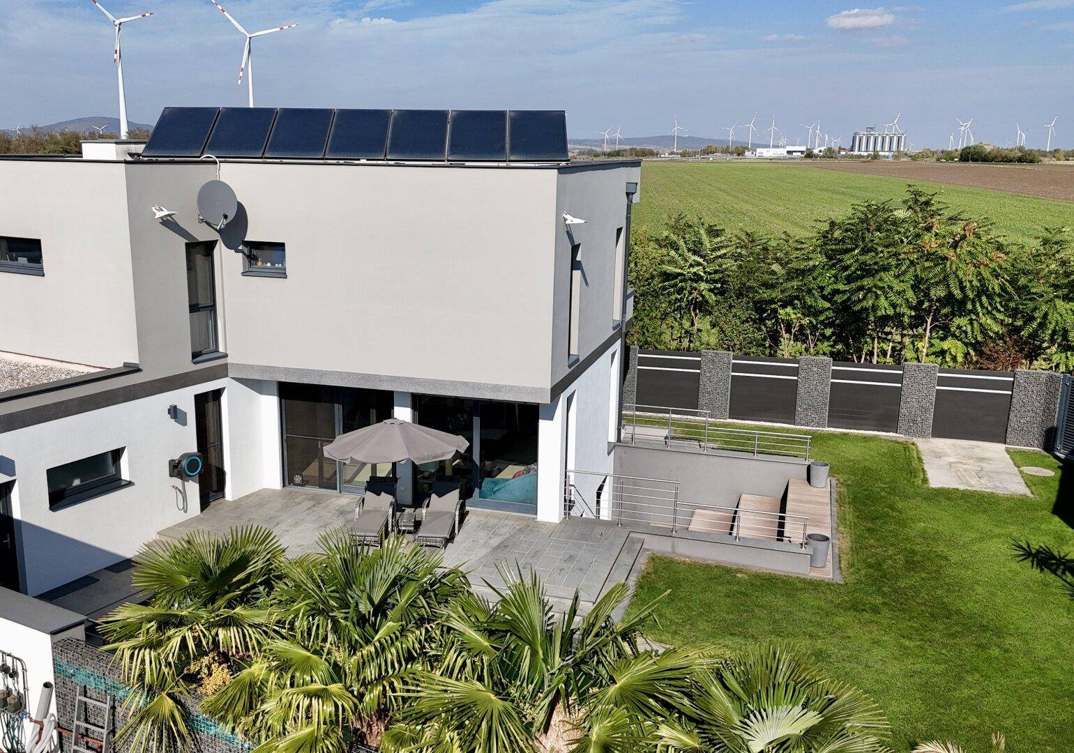 Luftaufnahme des modernen Hauses mit Pool, Garten und Blick auf Windräder.