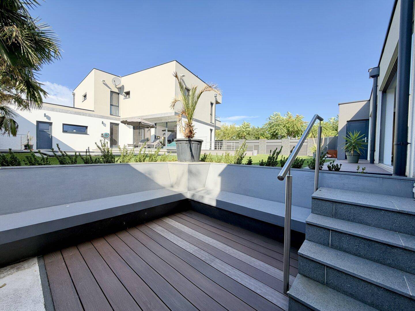 Moderne Terrasse mit Holzdeck, integrierter Sitzbank und Treppe zum Garten.