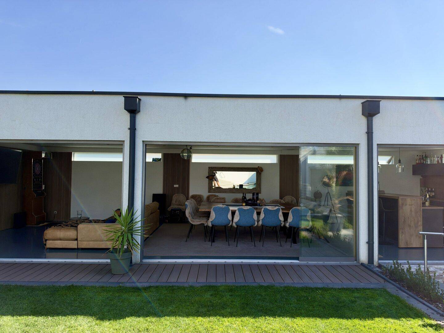 Offener Wohn- und Essbereich mit großen Glasfronten und Zugang zur Holzterrasse.