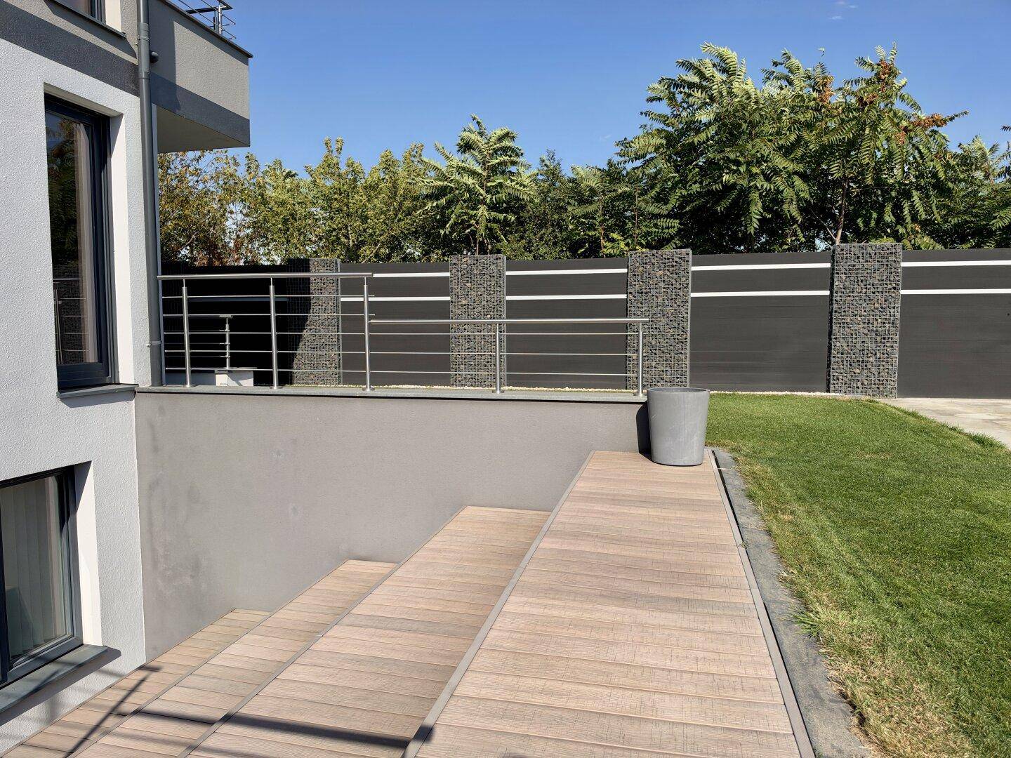 Gartenbereich mit Holzdeck, Treppen und modernem Zaun.