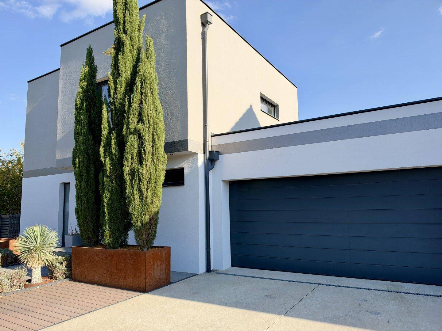 Elegante Hausfassade mit Zypressen in einem Cortenstahl-Pflanzgefäß und Garage.