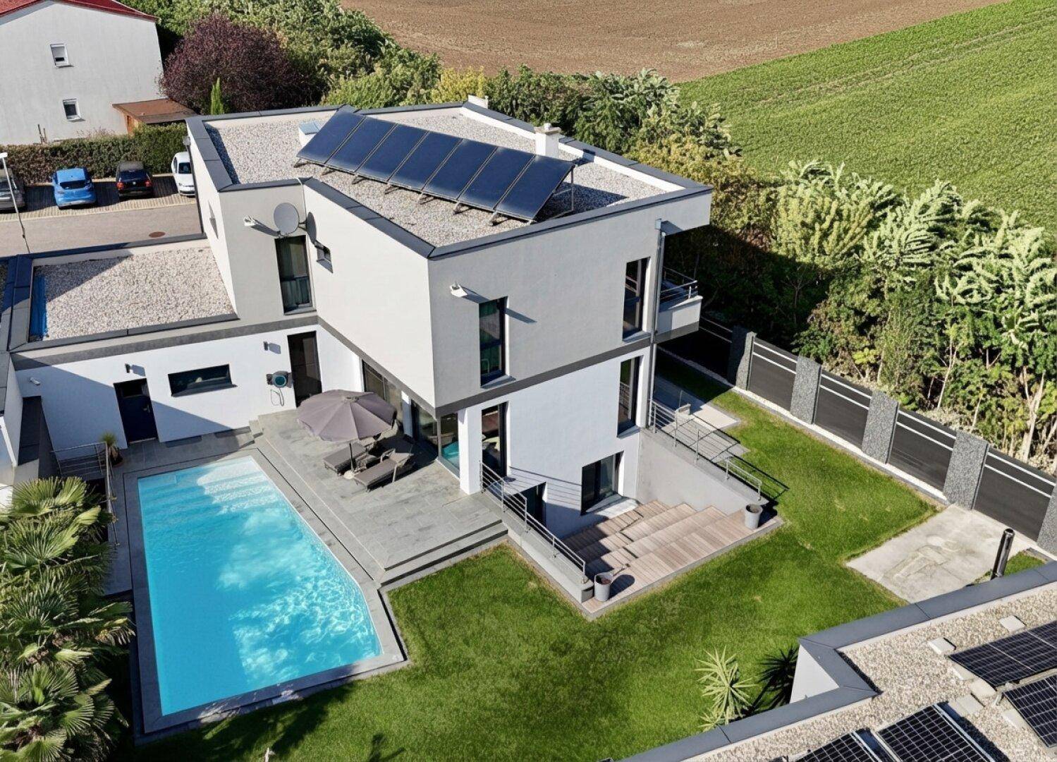 Luftaufnahme des modernen Hauses mit Pool, Garten und Photovoltaikanlage auf dem Flachdach.
