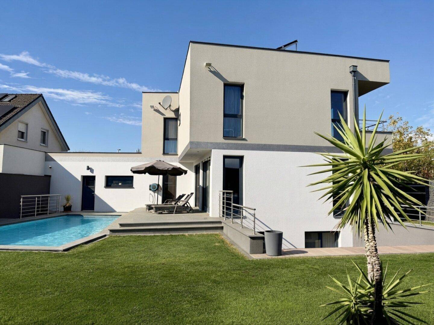 Modernes Einfamilienhaus mit Swimmingpool, sonniger Terrasse und gepflegter Rasenfläche.