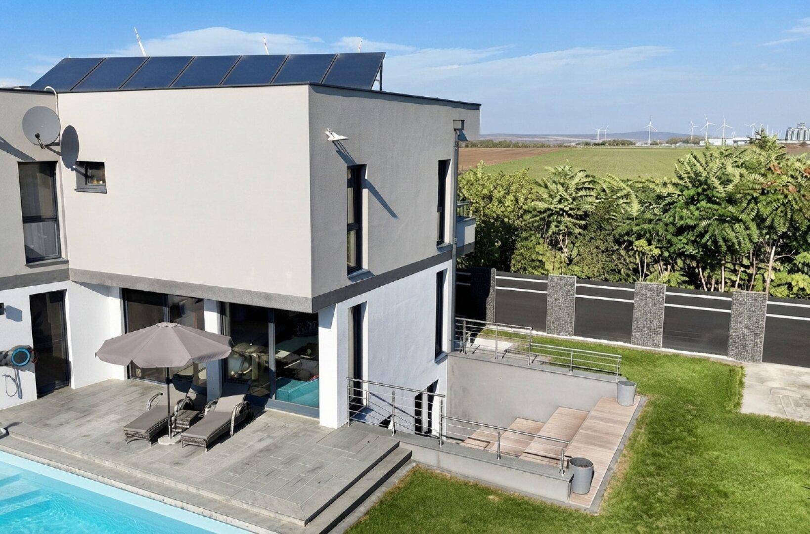 Rückseite des modernen Hauses mit Terrasse, Garten und weitem Blick auf die umliegende Landschaft.
