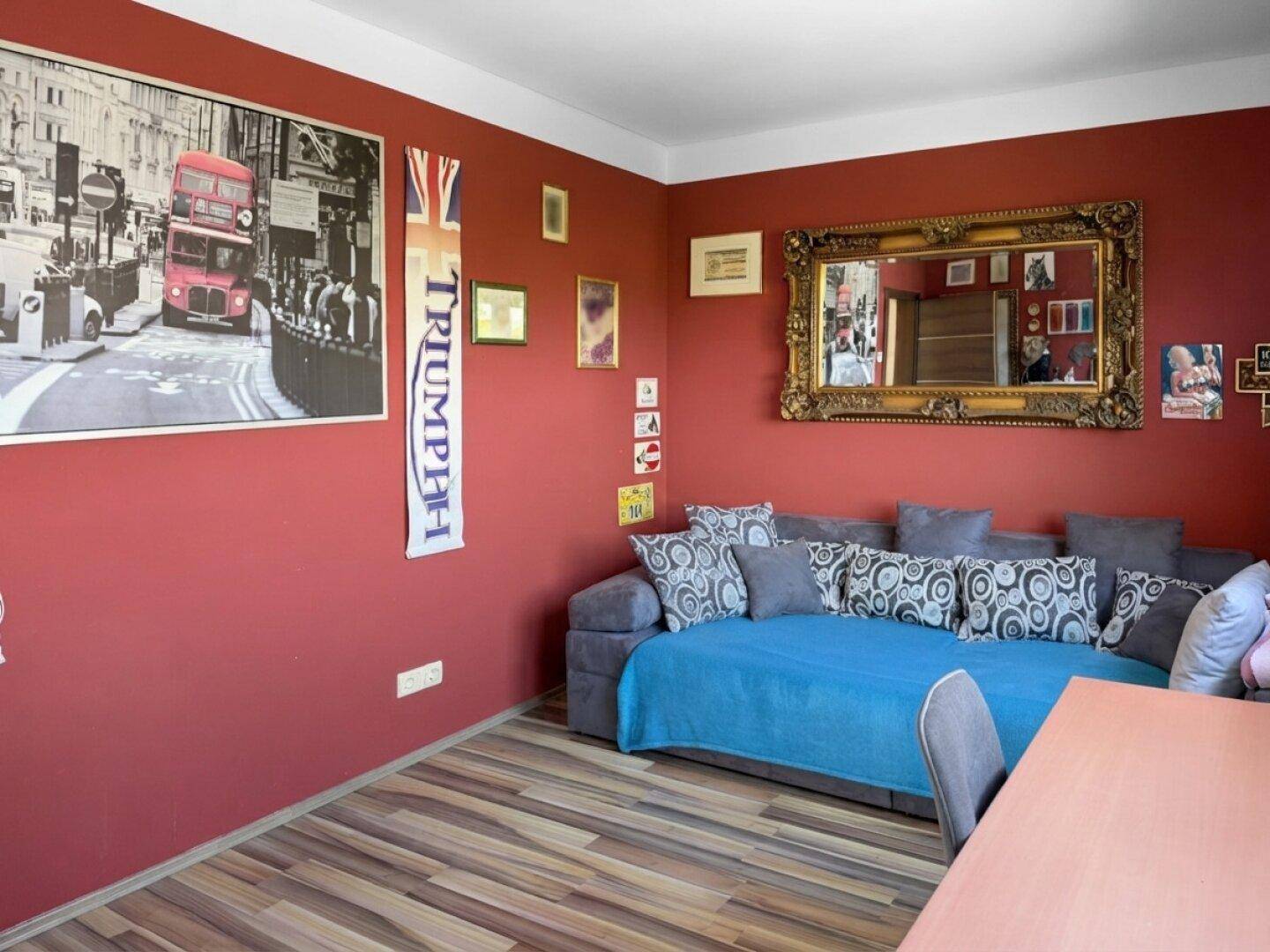 Lebhaftes Zimmer mit roter Wand, Schlafsofa und London-Dekoration, vielseitig nutzbar.