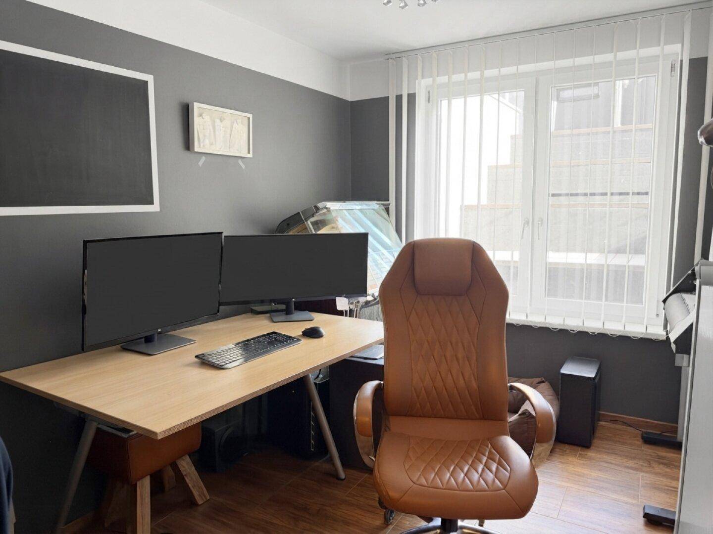 Modernes Arbeitszimmer mit zwei Monitoren, ergonomischem Stuhl und dunklen Wänden.