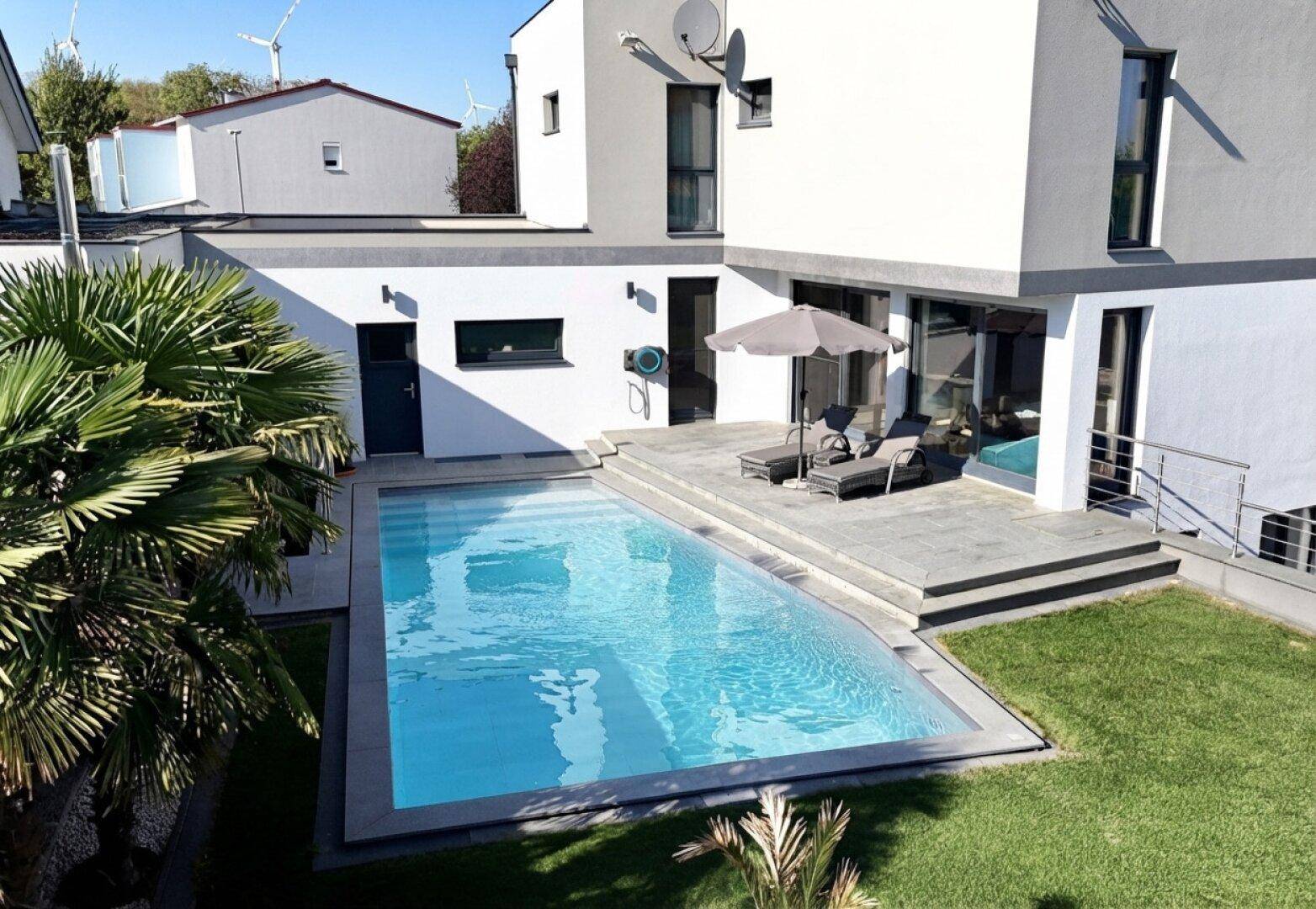Außenbereich mit großem Swimmingpool, Sonnenterrasse und Palmen.
