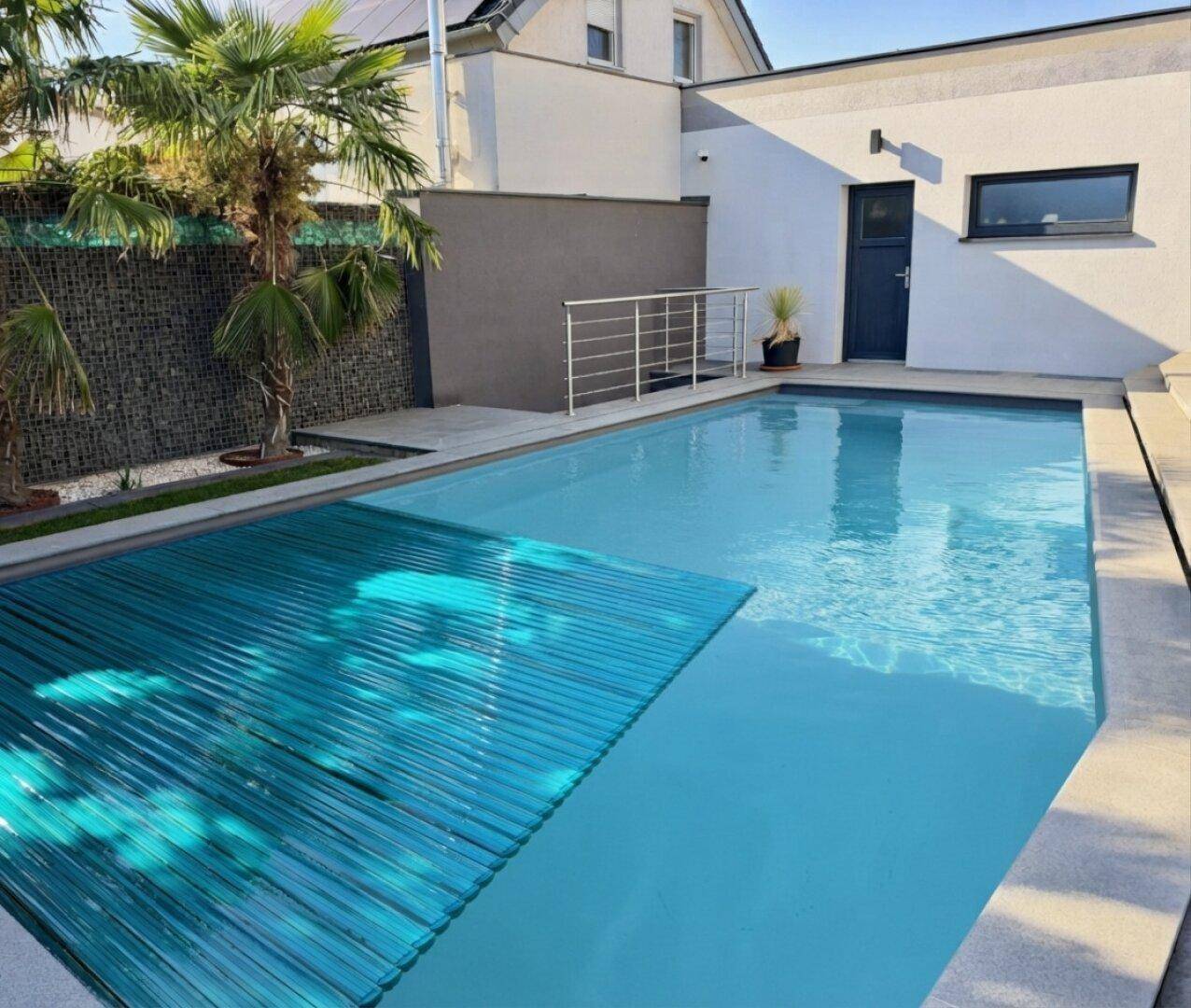 Moderner Außenpool mit blauer Abdeckung und Palmen in einem sonnigen Gartenbereich.