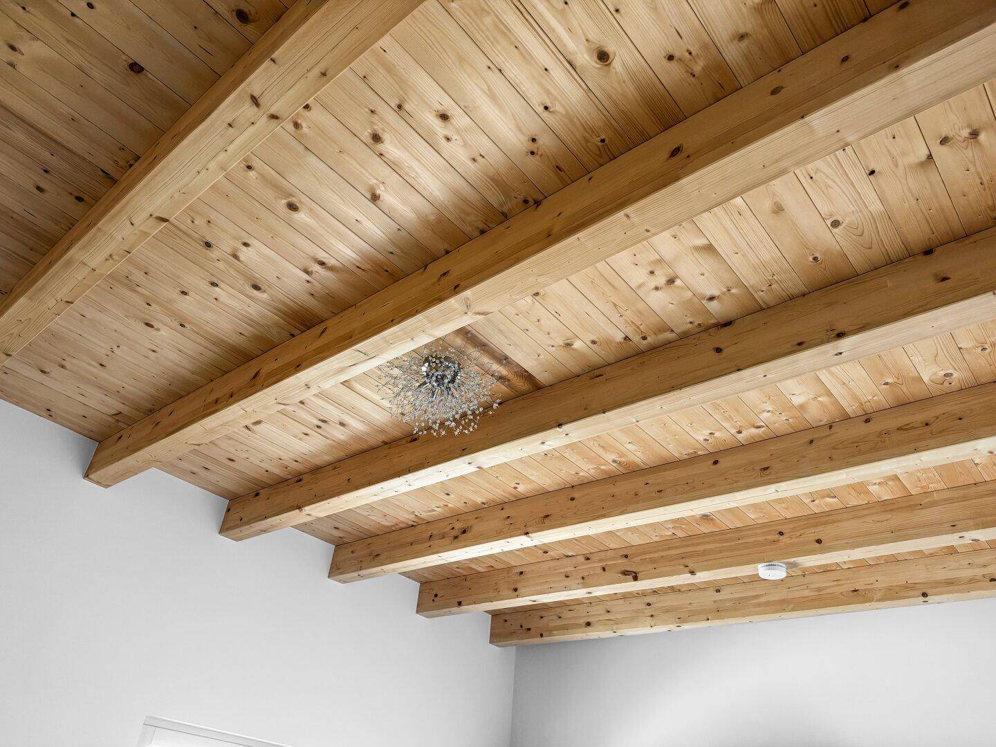 Detailaufnahme einer Holzbalkendecke mit moderner Beleuchtung, die Wärme und Charakter verleiht.