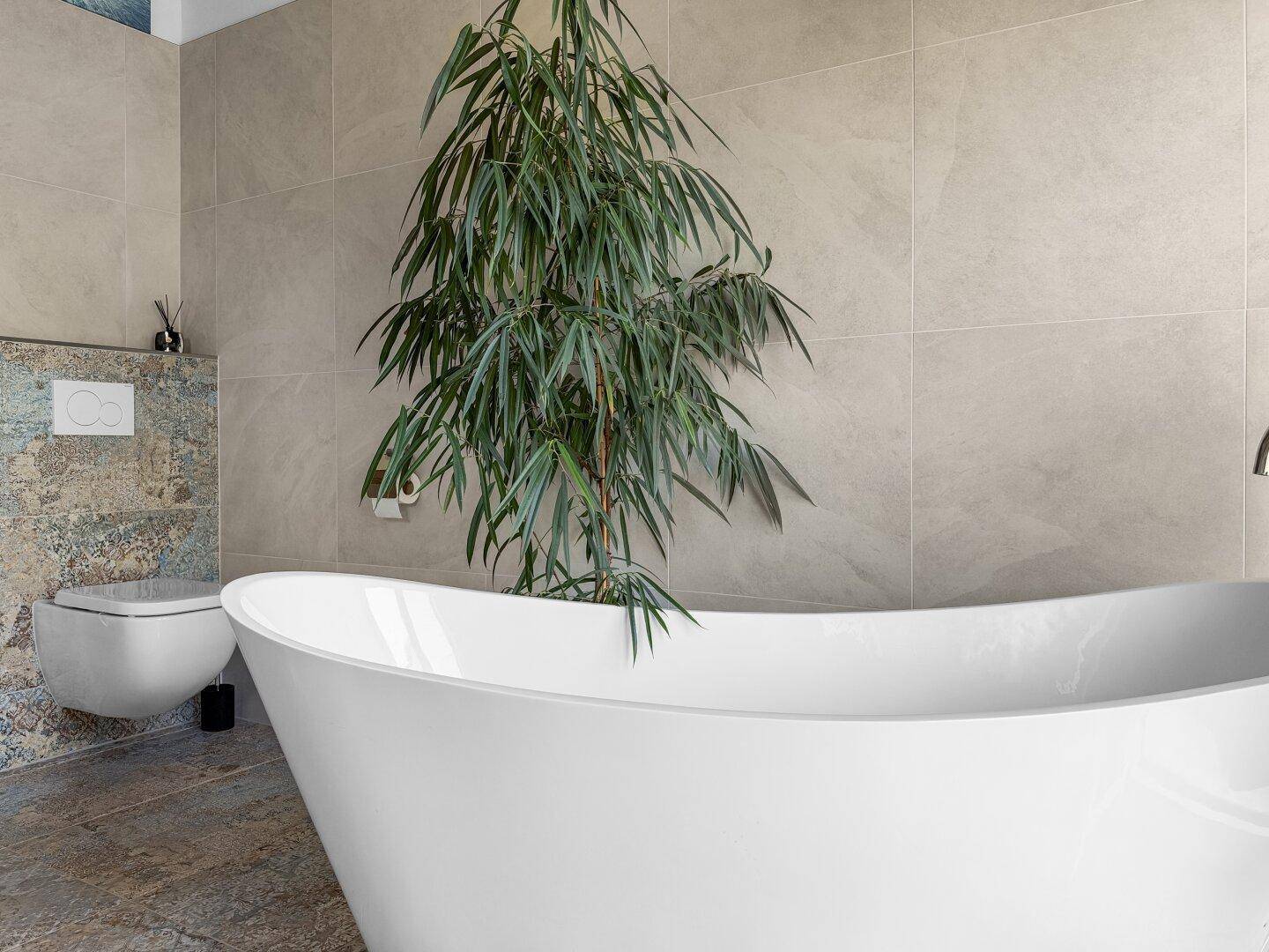 Freistehende Badewanne in einem modernen Badezimmer mit großen Fliesen und Pflanzen.