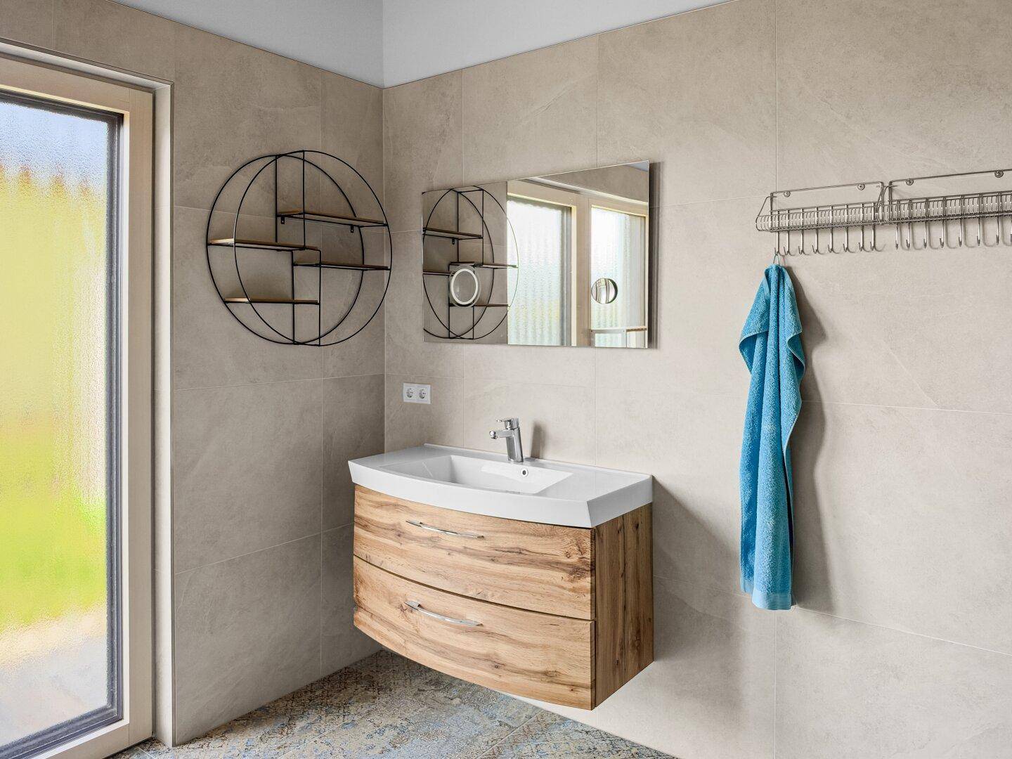 Modernes Badezimmer mit Holzwaschtisch, Spiegel und Fenster für natürliches Licht.